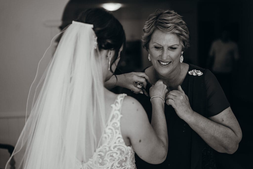 Documentary Style Getting Ready Photos. The bride helps her mother fasten her broach in an unscripted and intimate moment
