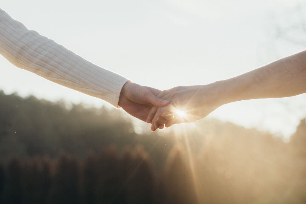 A couple holding hands while the sun streams behind them