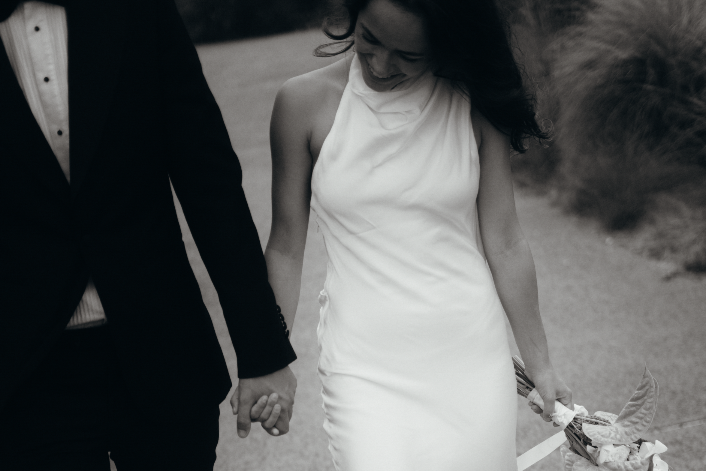 Luxurious couple casually walk while she laughs, gently holding her modern green and white bouquet by her side.