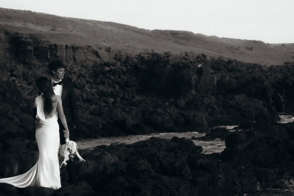 Black and white, dramatic photograph. Elegant couple poses on dark black rocks in Phillip Island Gippsland Victoria Australia.